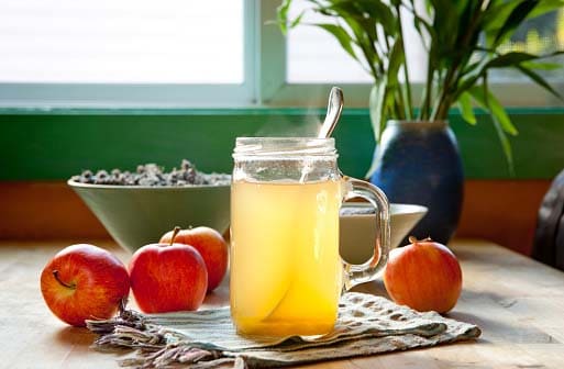 small glass jar filled with apple cider vinegar in warm water